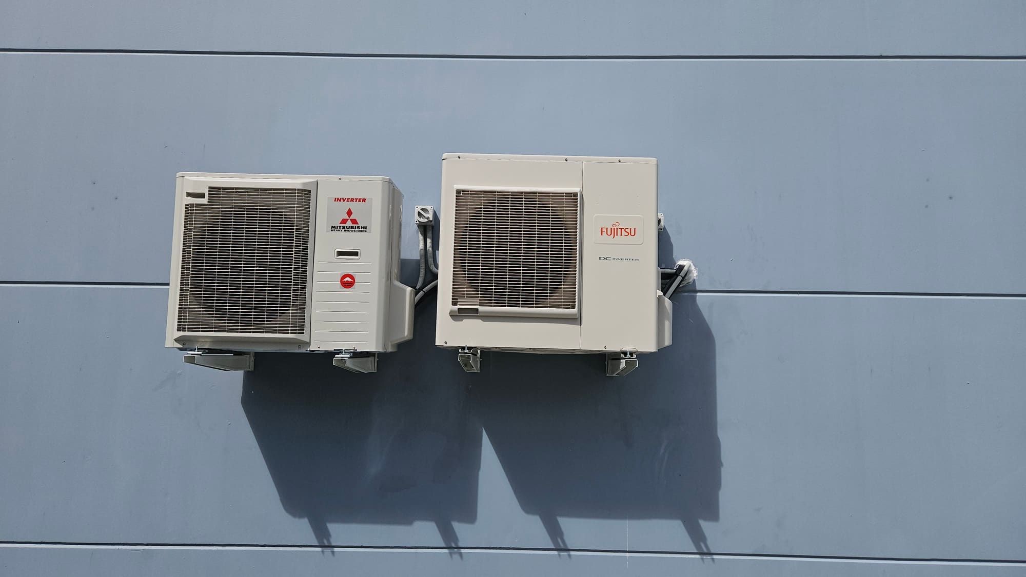 Two air conditioning outdoor units installed by AKO Air on a blue commercial wall